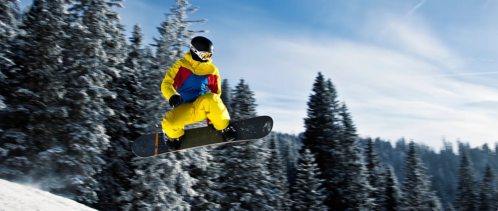 Un snowboardeur en vol au-dessus d’une pente enneigée, silhouette détachée sur le ciel